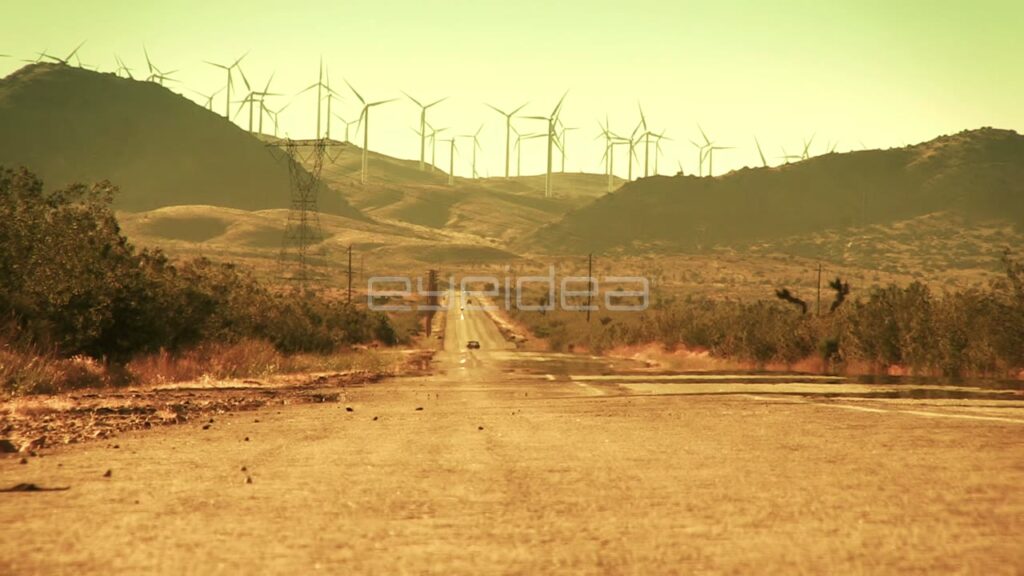 Car Driving on Desert Road with Wind Turbines in Golden Light